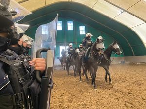 Po lewej stronie na pierwszym planie widoczni są policjanci z oddziałów prewencji. Na drugim planie po prawej stronie widoczni policyjni jeźdźcy na koniach służbowych idących dwójkami.