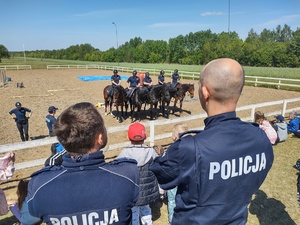 Policjanci z widowni razem z dziećmi oglądają pokaz policyjnych koni i ich jeźdźców