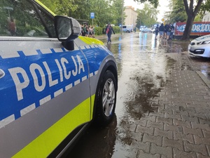Policyjny radiowóz stoi przy drodze zlanej deszczem po której chodzą kibice