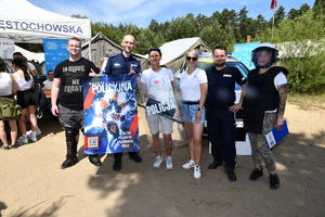 Policjanci i młodzież pozują do zdjęcia stojąc na tle radiowozu i wystawionych namiotów