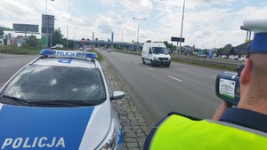 Policyjny radiowóz a przy nim policjant przy drodze kontroluje prędkość pojazdów