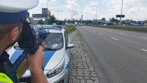 Droga, przy której stoi radiowóz i policjant, mierzący prędkość pojazdów