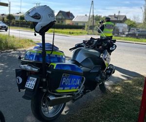 Policyjny motocykl stoi przy drodze a policjant patroluje drogę