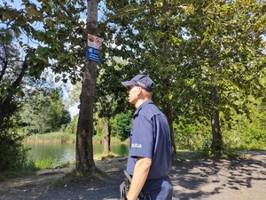 Policjant sprawdza oznaczenia o zakazie kąpieli nad zbiornikiem