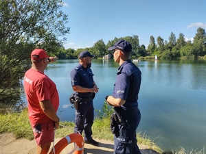 Policjanci rozmawiają z ratownikiem nad brzegiem akwenu