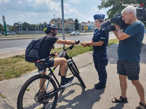 Policjantka rozmawia z rowerzysta, a operator kamery nagrywa