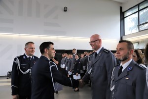 Policjanci stoją w szeregu, a komendant podaje rękę jednemu z nich i składa gratulacje