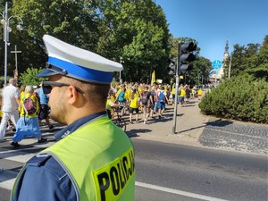 Policjant stoi na drodze i zabezpiecza przejście przez jezdnie pielgrzymów