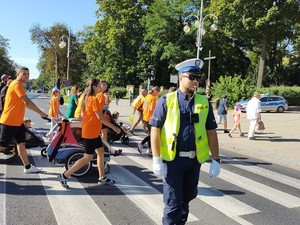 Pielgrzymi przechodzą przez jezdnię, a policjant zabezpiecza to miejsce