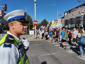 Policjant czuwa nad bezpieczeństwem przechodzącej przez jezdnie pielgrzymki