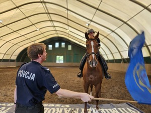 Policjant wymachując flagą symuluje zagrożenie dla policjantki jadącej na koniu