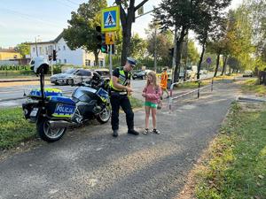 Policjant przy przejściu dla pieszych wręcza opaskę odblaskową dziewczynce