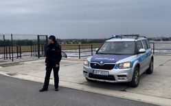 Na zdjęciu widoczny policjant stojący obok radiowozu.