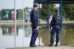 Na zdjęciu widoczna policjantka i policjant, którzy przyglądają się podtopionemu terenowi.