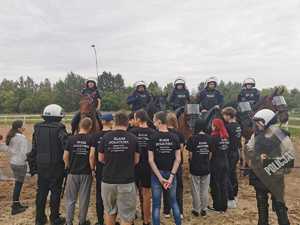 Młodzież stoi zwrócona w kierunku policjantów siedzących na koniach