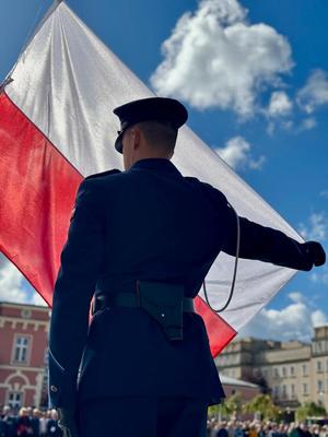 Policjant trzyma ręką flagę Polski, która jest rozłożona