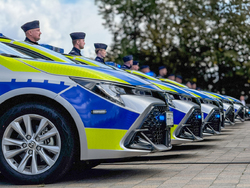 Policjanci stoją przy nowych radiowozach zaparkowanych na parkingu