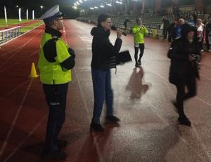 Policjant stoi wśród zawodników na bieżni stadionu