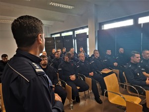 Policjanci siedzą w ławkach i słuchają tego co mówi komendant