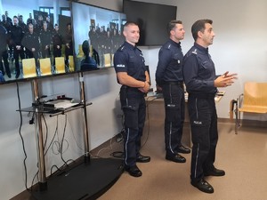 Komendant i policjanci stoją przy monitorach, które wyświetlają obraz