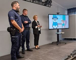 Policjanci i kobieta stoją przy rzutniku na którym wyświetla się film