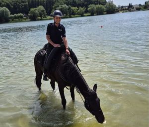 Policjantka na koniu w zbiorniku wodnym z którego koń pije wodę