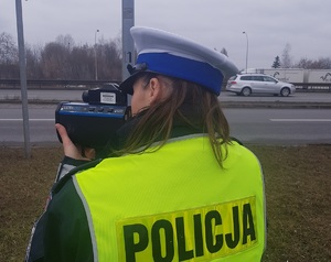 Policjantka na drodze urządzeniem mierzy prędkość pojazdów