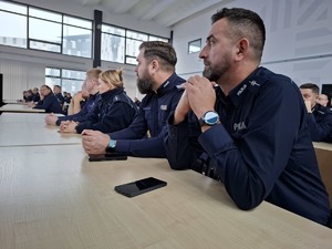 Policjanci w umundurowaniu służbowym siedzą w ławkach i słuchają wykładu