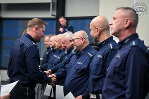 Policjant spośród stojących w szeregu policjantów ściska dłoń jednemu z nich i składa gratulacje