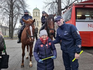 Seniorka z policjantem pozuje do zdjęcia, w tle policyjne konie