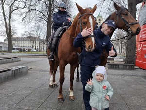 Policjant z dziewczynką pozuje do zdjęć na tle policyjnych koni