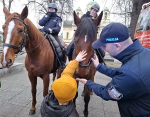 Dziecko głaszczę konia po łbie, obok asystuje policjant