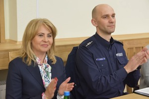 Policjant siedzi obok kobiety i klaszcze w dłonie