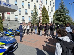 Policjant przy radiowozach rozmawia z ludźmi przed komendą