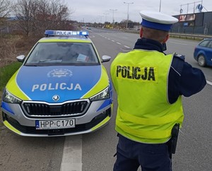Policjant przy radiowozie stoi przy drodze