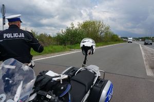 Policjant patroluje ruch pojazdów, obok niego stoi zaparkowany policyjny motocykl