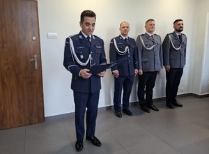 Policjanci w umundurowaniu galowym stoją w sali, a komendant przemawia