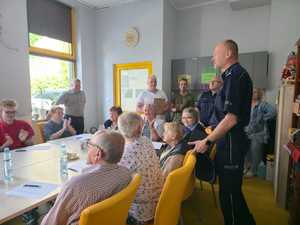 Policjant rozmawia z seniorami, którzy siedzą przy stolikach