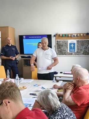 Mężczyzna rozmawia z seniorami, obok stoi umundurowany policjant