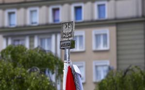 Głowica sztandaru z orłem w koronie na tle budynku