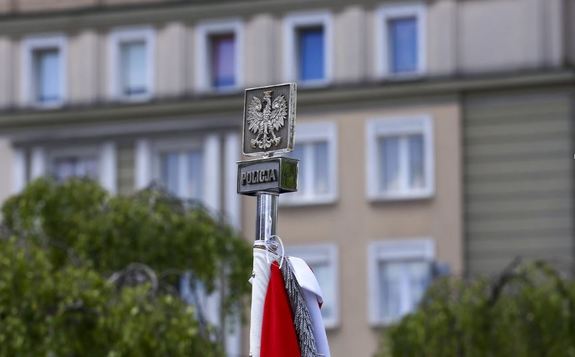 Głowica sztandaru z orłem w koronie na tle budynku