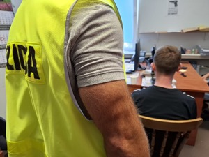 Podejrzany w pokoju służbowym podczas przesłuchania. Za nim stoi policjant