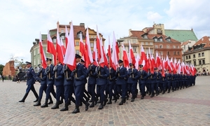Policjanci w umundurowaniu galowym maszerują i prezentuje sztandar