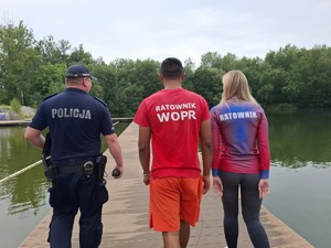 Policjant i dwóch ratowników idą pomostem przy zbiorniku wodnym