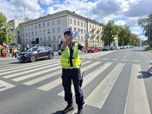 Policjant na drodze wykonuje gest rękami w stronę kierujących