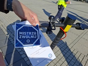 Ulotka informacyjna z napisem: mistrzu zwolnij trzymana na kierownicy hulajnogi