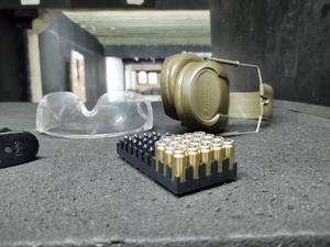 Naboje w koszyczku z okularami i słuchawkami na tle tarczy celowniczej