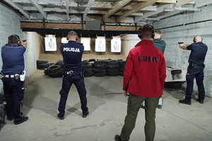 Policjanci celują z broni do tarczy, za nimi stoi instruktor