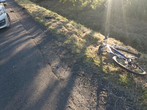 Wywrócony rower na pobocze, obok na drodze stoi zaparkowany policyjny radiowóz