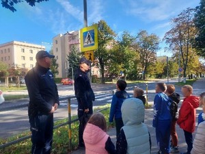 Dzielnicowi z grupą dzieci rozmawiają przy przejściu dla pieszych